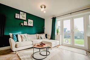 A modern living room with a sectional sofa, a coffee table, and a large window with curtains. - Host & Stay | Mercia House (Kempsey)