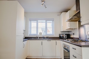 A kitchen with white cabinets, a window, a microwave, and a stove. - Host & Stay | Mercia House (Kempsey)