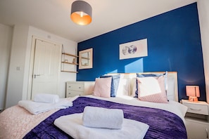 A bedroom with a bed, a nightstand, a lamp, a mirror, and a door.