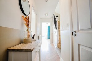 A hallway with a wooden counter, a vase with dried flowers, a mirror, and a staircase leading to another room. - Host & Stay | Mercia House (Kempsey)