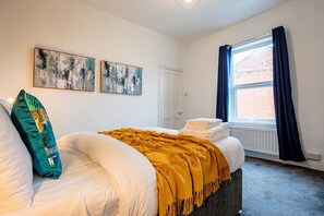 A bedroom with a bed, two wall-mounted abstract paintings, a window with blue curtains, and a radiator.