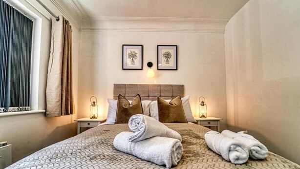 Een keurig opgemaakt bed met een gestructureerd sprei, twee ingelijste kunstwerken erboven en twee bedlampjes.