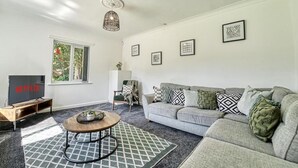 Een woonkamer met een grijze bank, een salontafel, een televisie en kunstwerken in lijsten aan de muur.
