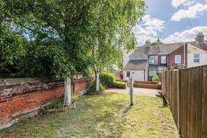 A residential backyard with a brick wall, a wooden fence, and a large tree. - Host & Stay | The Haven at Church Road (Gorleston-on-Sea)