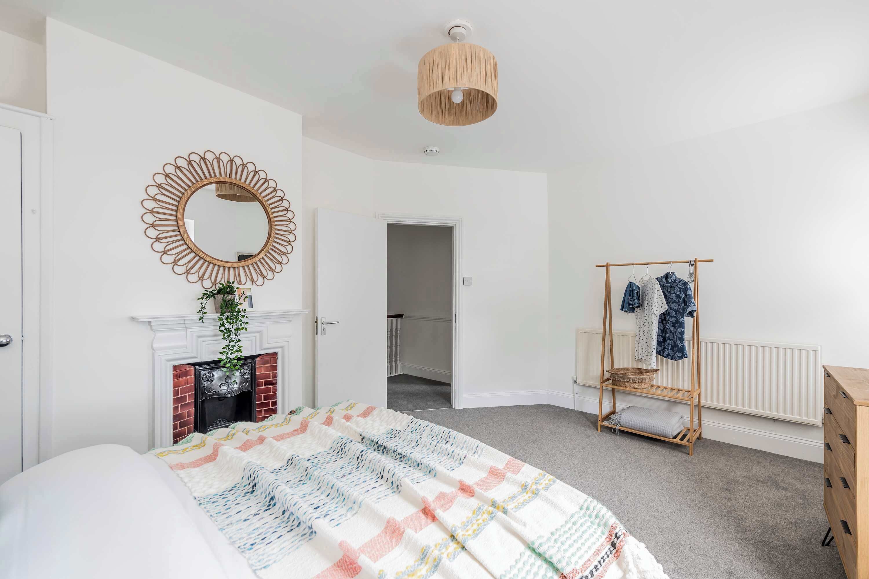 Een slaapkamer met een bed, een spiegel, een hanglamp, een radiator en een kledingrek.