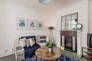 A living room with a sofa, a coffee table, a hanging floor lamp, and a fireplace. - Host & Stay | The Haven at Church Road (Gorleston-on-Sea)