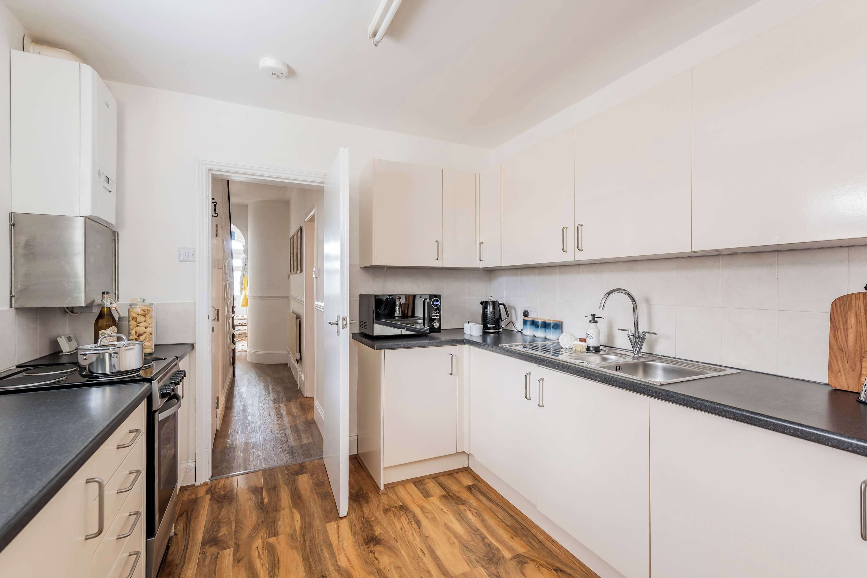 Een moderne keuken met witte kastjes, een roestvrijstalen spoelbak en een houten vloer.