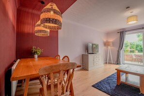 A dining area with a wooden table and chairs, a TV on a cabinet, and a large window with curtains. - Host & Stay | Hales Orchard (Worcester)