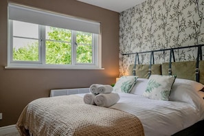 A bedroom with a large window, a bed with rolled towels, and patterned wallpaper. - Host & Stay | Hales Orchard (Worcester)