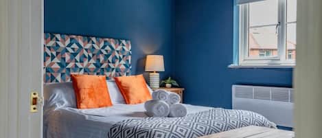 Une chambre à coucher avec un lit, des oreillers, une table de chevet, une lampe et une fenêtre.