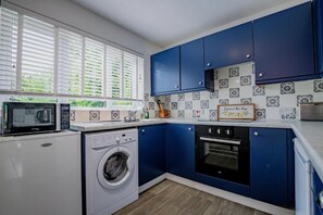 A compact kitchen with a washing machine, microwave, oven, and blue cabinets. - Host & Stay | Hales Orchard (Worcester)