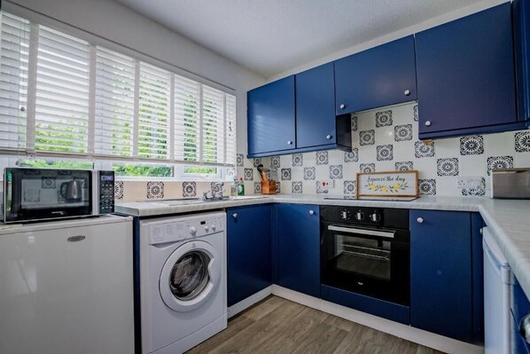 Une cuisine compacte équipée d’un lave-linge, d’un four à micro-ondes, d’un four et de meubles de couleur bleue.