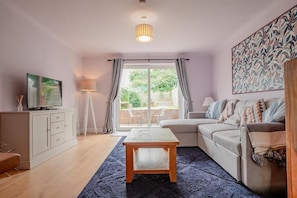 A living room with a sofa, a coffee table, a TV on a cabinet, and a large window with curtains. - Host & Stay | Hales Orchard (Worcester)