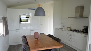 A modern kitchen with white cabinets, a wooden dining table with chairs, a pendant light, and a built-in oven.