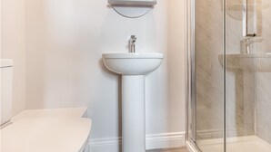 A bathroom with a white pedestal sink, a mirror above it, and a glass shower enclosure.