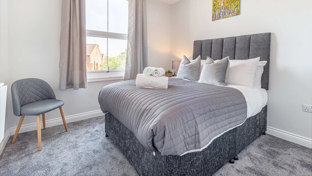 A bedroom with a large bed, a chair, a window with curtains, and a painting on the wall.