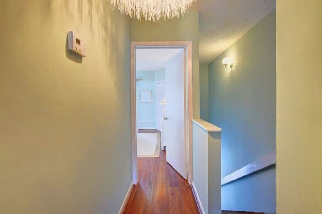 A narrow hallway with wooden flooring, a light switch on the wall, and a door leading to another room.
