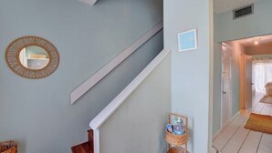 Una escalera con una pared azul claro, un espejo redondo y un pequeño marco de fotos. Hay una cesta con objetos en el suelo, cerca de la escalera.
