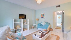 Una sala de estar con un sofá, una mesa de centro, un televisor y una estantería.