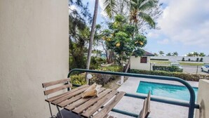 Un balcón con mesa y sillas de madera, con vista a una piscina y abundante vegetación.