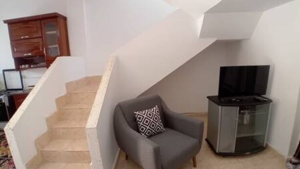 Un salon avec un fauteuil gris, un meuble TV noir et un buffet en bois.