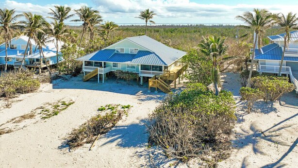 A beachfront property with multiple houses, each featuring a blue roof and white walls, surrounded by palm trees and sandy beach. - Gulf Front Getaway at Gulf Cottage 1108 (Captiva)