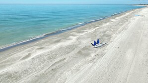 An aerial view of a beach with clear skies, calm waters, and a few beach chairs and umbrellas. - Gulf Front Getaway at Gulf Cottage 1108 (Captiva)