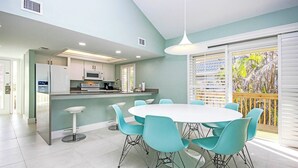A modern kitchen with a central island, white cabinets, and a dining area with a round table and teal chairs. - Gulf Front Getaway at Gulf Cottage 1108 (Captiva)