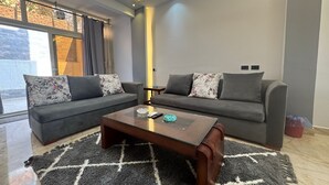 A modern living room with two grey sofas, a wooden coffee table, and a patterned rug. - 129 · 2BR Townhouse, 2 Bath, TV, Backyard (Sheikh Zayed City)
