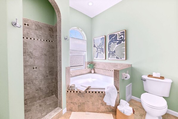 A bathroom with a shower, bathtub, toilet, and two wall-mounted artworks.