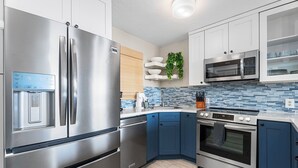 A modern kitchen with stainless steel appliances, blue cabinets, and a tiled backsplash. - Kailua Village#705 Top Floor, Gorgeous Remodeled 2 bedroom, in Heart of Town (Kailua Kona)