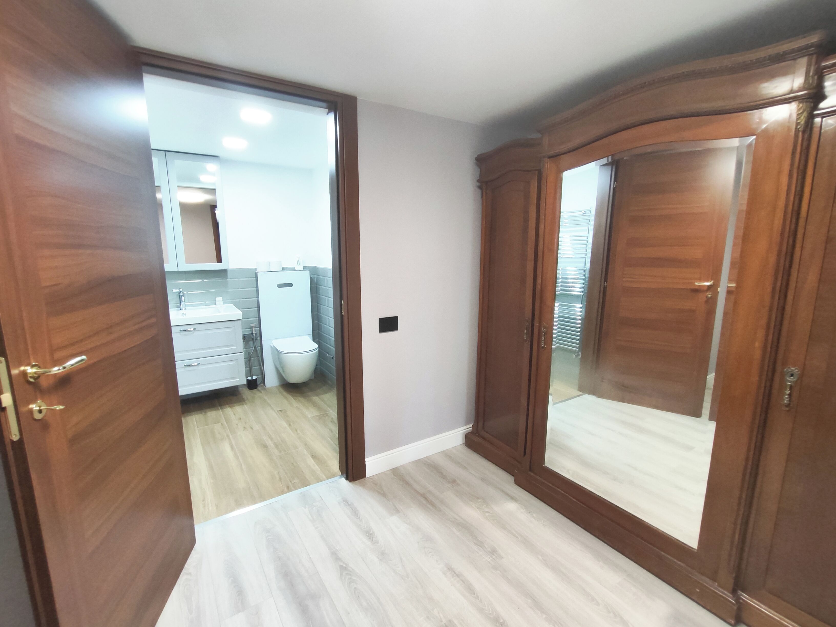 A hallway with wooden doors, a white toilet, and a sink.