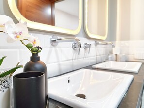 Un bagno con due lavandini, uno specchio e un vaso con orchidee bianche.
