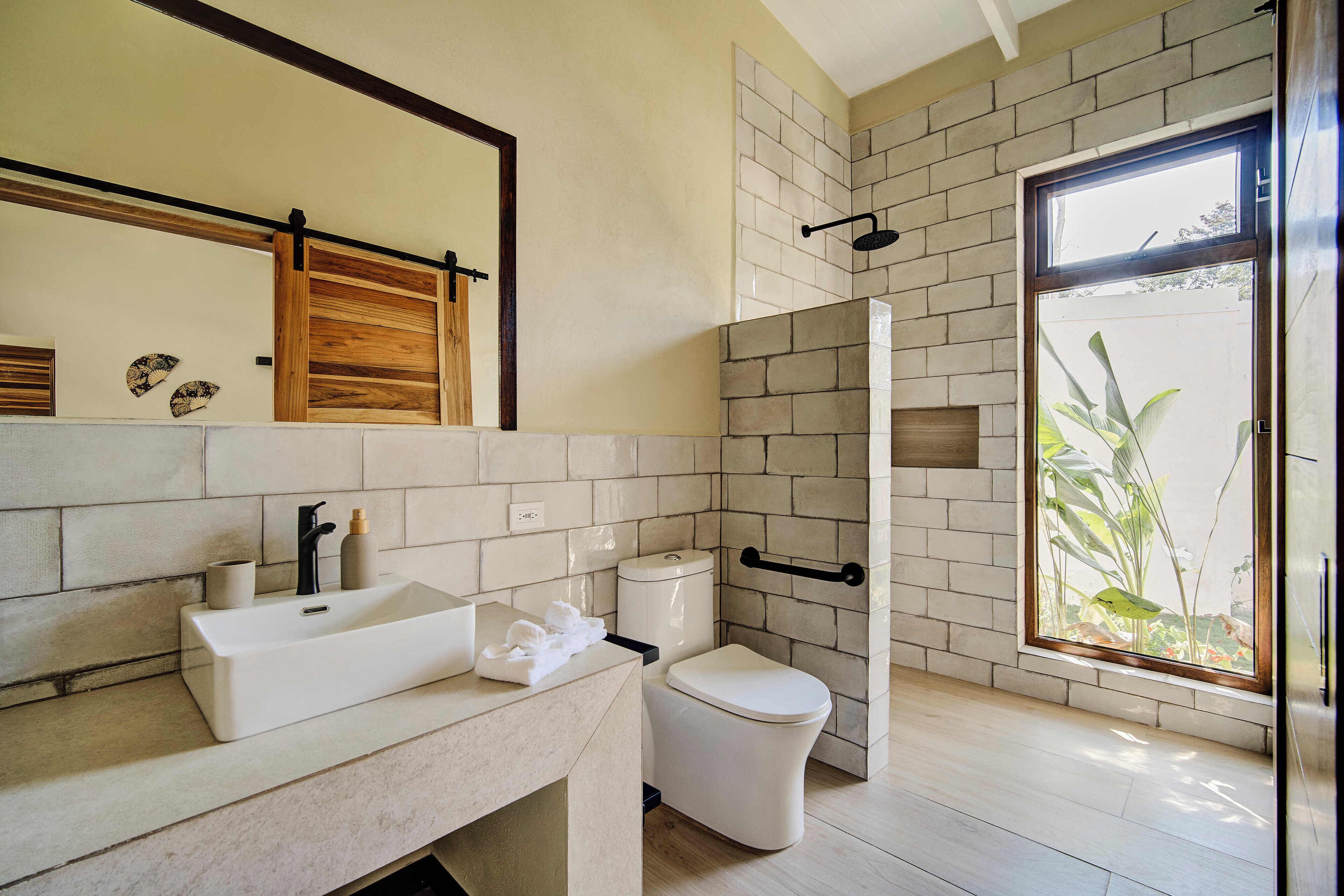 Een moderne badkamer met een groot raam, een witte wastafel, een toilet en een douche.