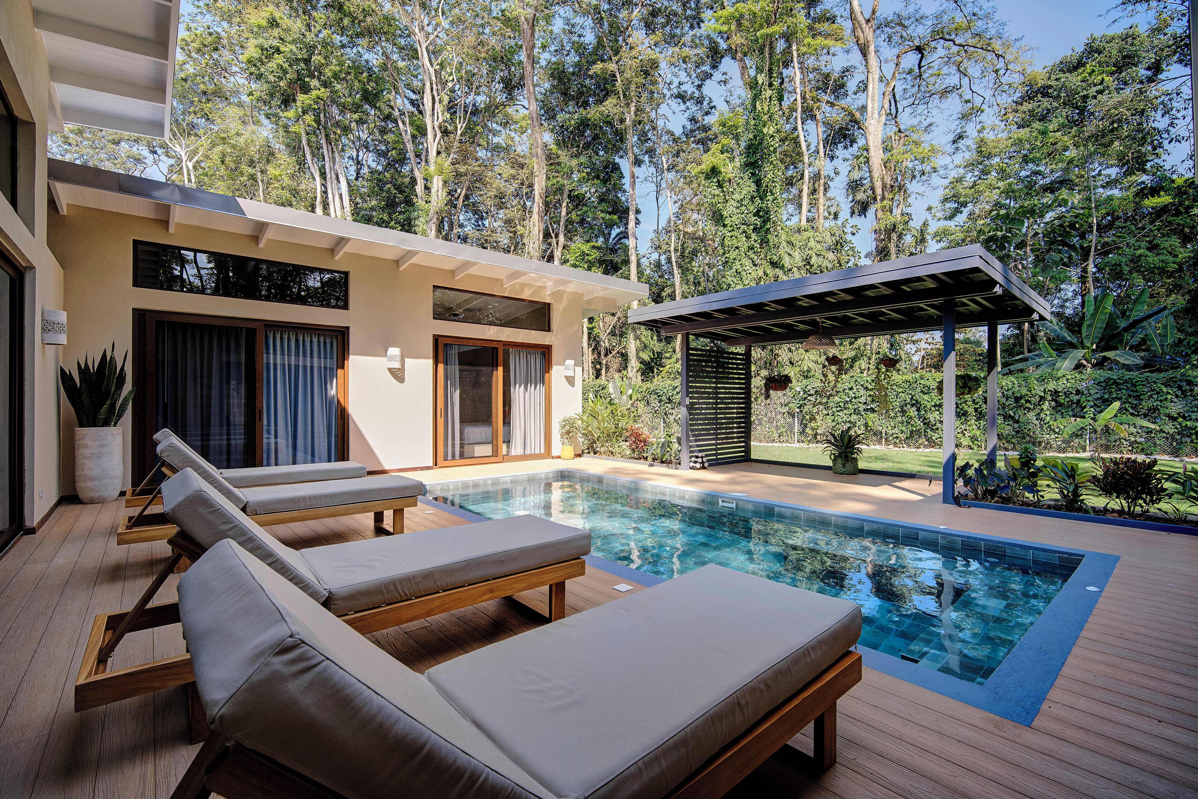 A modern outdoor pool area with lounge chairs, a wooden deck, and a covered seating area.