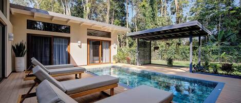 A modern outdoor pool area with lounge chairs, a wooden deck, and a covered seating area.