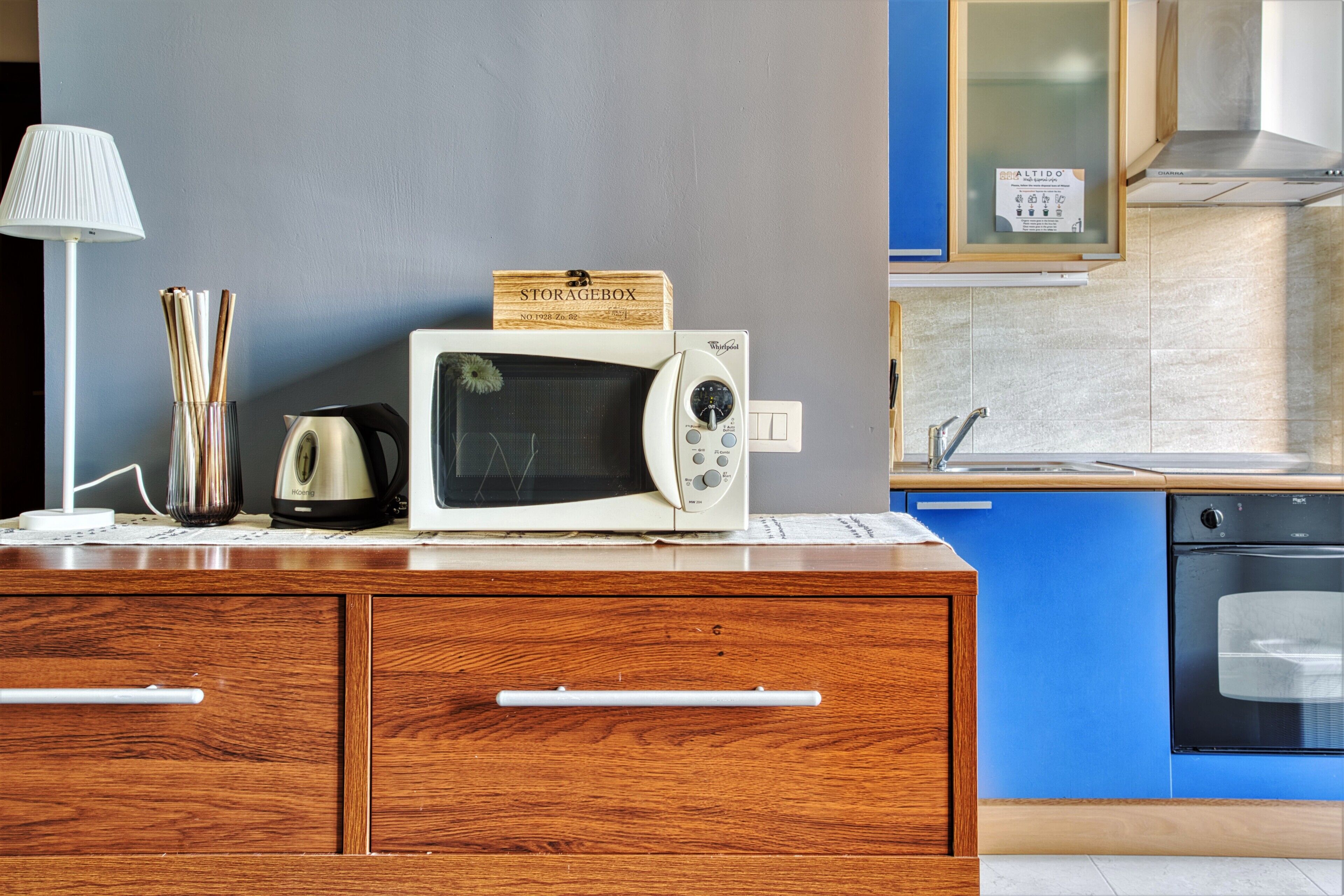 Une petite cuisine équipée d’un four à micro-ondes, d’une bouilloire et d’une boîte de rangement, le tout placé sur un meuble en bois.