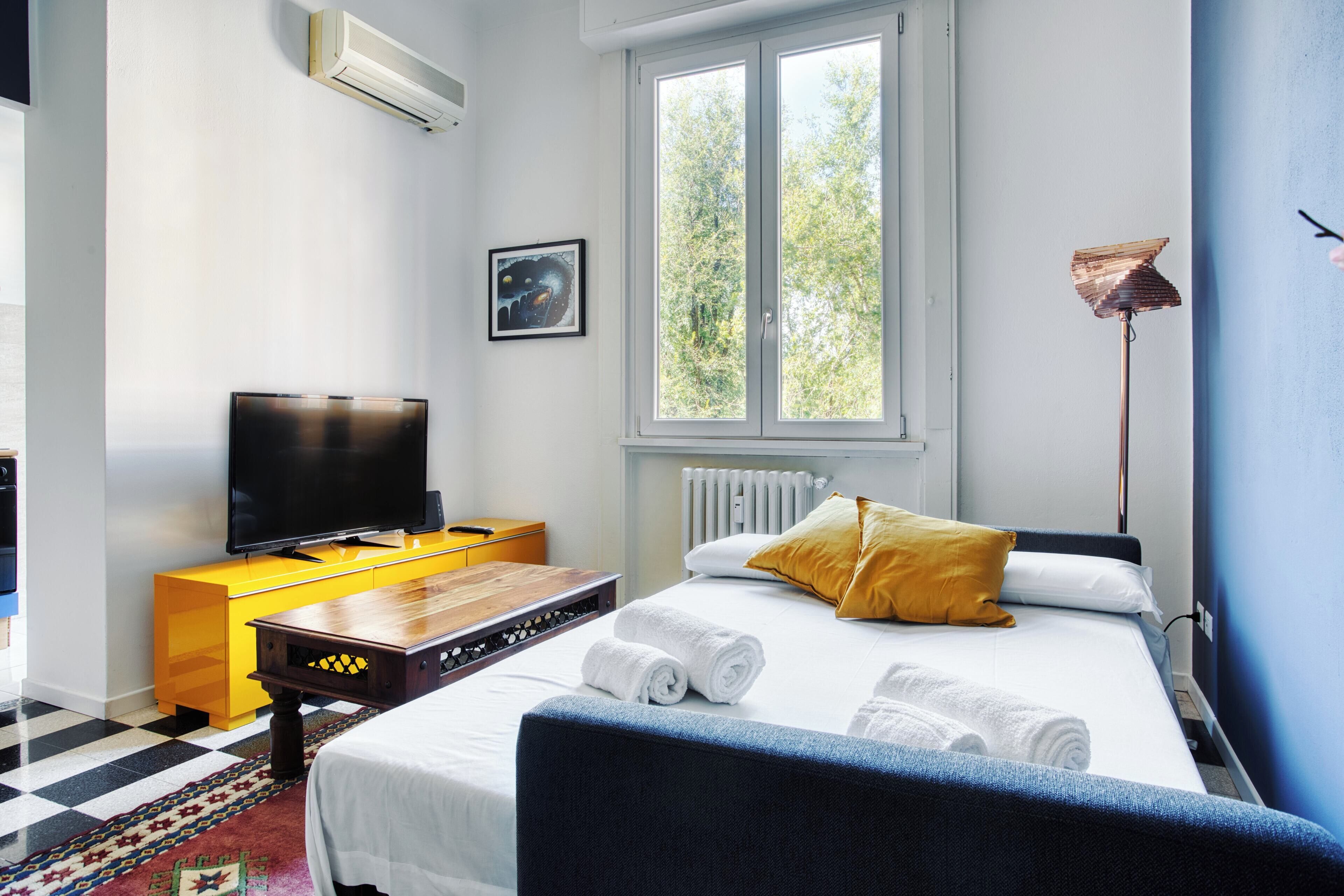 A hotel room with a bed, a television, a window, and a radiator.