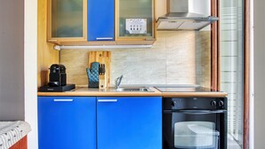 A compact kitchen with blue cabinets, a coffee maker, a knife block, and a built-in oven. - JOIVY Stylish Flat in Porta Genova (Milan)