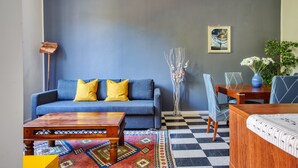 A modern living room with a blue sofa, a wooden coffee table, a patterned rug, and a checkered floor. - JOIVY Stylish Flat in Porta Genova (Milan)