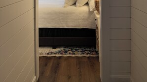 Een kamer met een laag, schuin dak, een bed, een ronde spiegel en een klein raam.