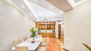 A dining area with a long table, chairs, and a vase of flowers. There is a kitchen in the background with wooden cabinets and a microwave. - Stay Inn on North 11 (Yerevan)