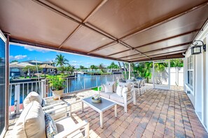 A covered outdoor patio with a pool view, white furniture, and a potted plant. - Heated Pool! Waterfront+Kayak! Close 2 Beach! (Pompano Beach)
