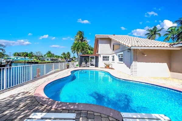 A swimming pool with a curved edge, surrounded by a white fence and a paved deck. - Heated Pool! Waterfront+Kayak! Close 2 Beach! (Pompano Beach)
