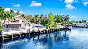 A waterfront property with a dock extending into a calm body of water, surrounded by lush greenery and palm trees. - Heated Pool! Waterfront+Kayak! Close 2 Beach! (Pompano Beach)