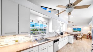 A modern kitchen with white cabinets, a large window, and a ceiling fan. - Heated Pool! Waterfront+Kayak! Close 2 Beach! (Pompano Beach)