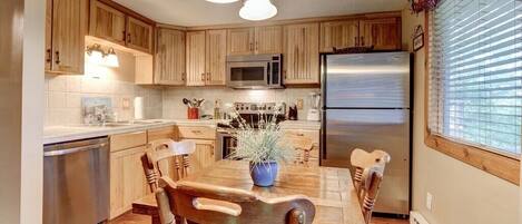 A kitchen with wooden cabinets, a stainless steel refrigerator, a microwave, and a dining table with chairs.