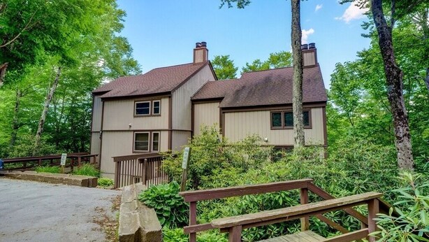 A two-story building with a wooden deck in front, surrounded by lush greenery.
