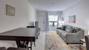 A modern living room with a dark wooden dining table, a grey sofa, and a colorful rug. - Modern condo: Steps from Atlantis & Beach (Bayview Lane)