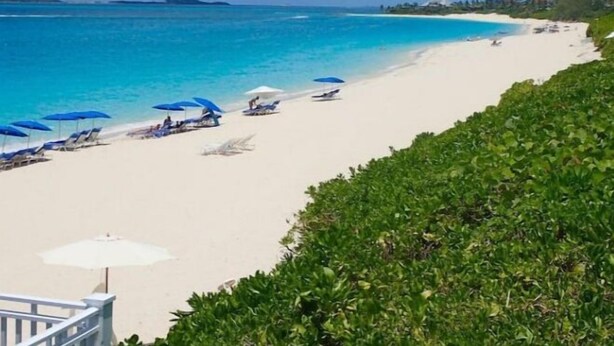 A beach with white sand, clear blue water, and a few umbrellas. - Modern condo: Steps from Atlantis & Beach (Bayview Lane)